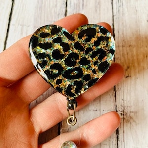 Puede incluir: Un portagafete en forma de coraz&oacute;n con estampado de leopardo, con un carrete de gafete retr&aacute;ctil transparente y un dije de cristal brillante.