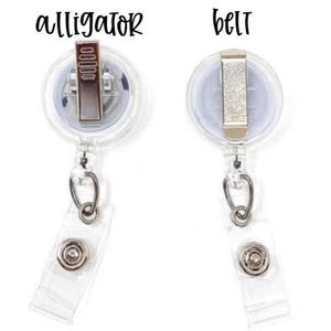 Pu&ograve; includere: Due porta badge retrattili trasparenti con clip in metallo. Uno &egrave; etichettato "alligator" e l'altro "belt" in corsivo nero. Ognuno ha un cinturino in plastica trasparente con chiusura a scatto e un anello in metallo color argento.