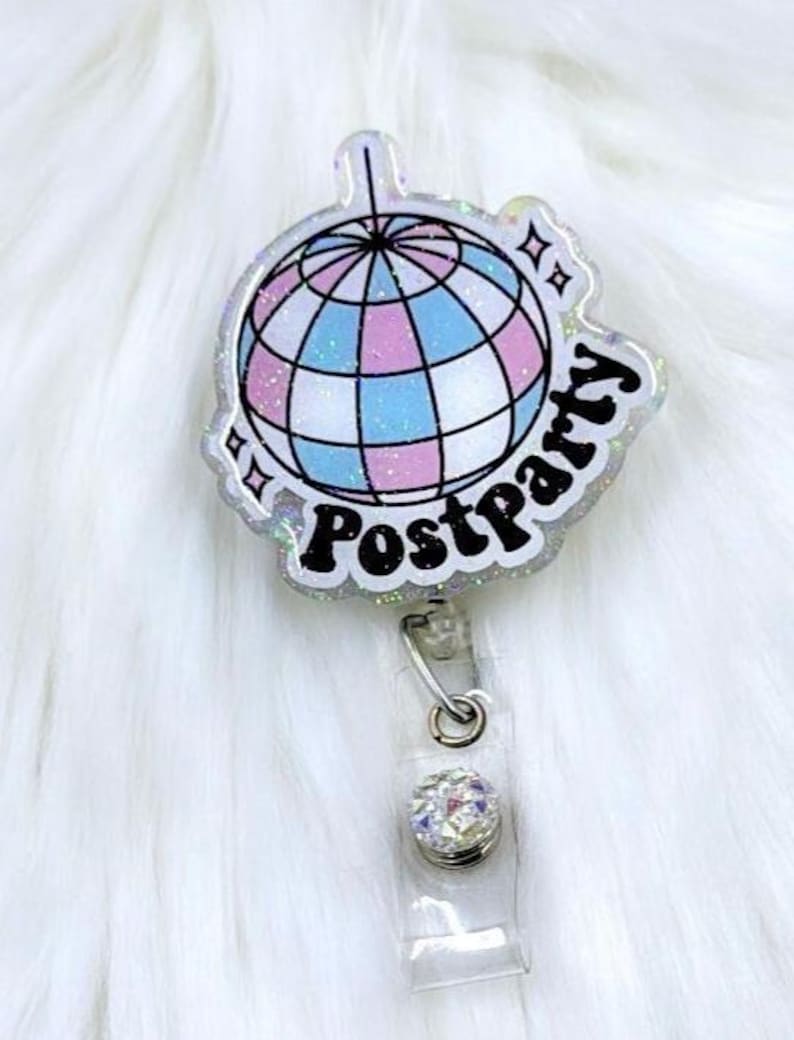 May include: A clear acrylic badge reel featuring a glittery disco ball graphic with pink and blue panels. The text "Postparty" is printed in bold black letters below the disco ball, accompanied by small star icons on a shimmering, translucent base.