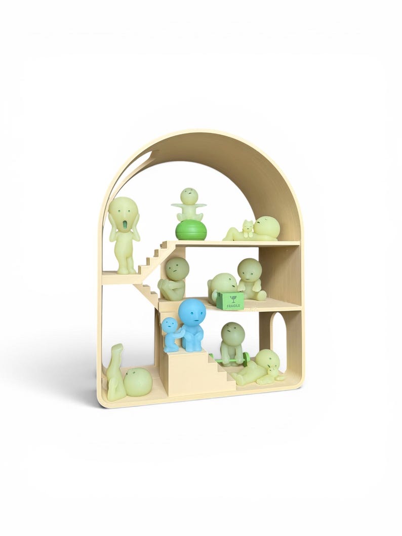 May include: A wooden dollhouse-style shelf filled with various small, stylized figurines in shades of green and blue. The shelf has an arched top and multiple levels, with the figurines arranged on the steps and shelves. Some figurines are in the shape of people.