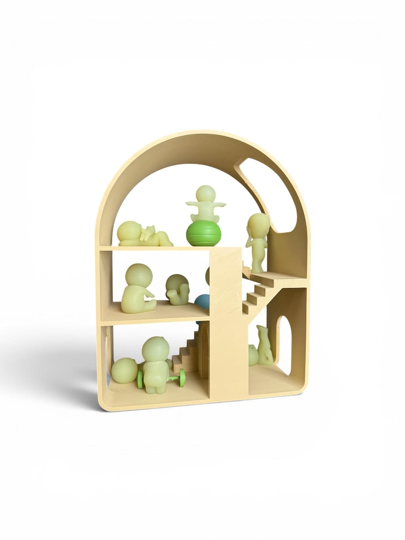 May include: A light beige wooden dollhouse with multiple levels and a curved roof. The dollhouse is furnished with small, green-tinted figurines in various poses. Some figurines are standing, sitting, or lying down. A green ball and a green toy with wheels are also present.