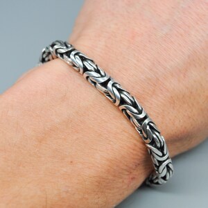 Może przedstawiać: Srebrna bransoletka z łańcuszkiem typu box. Bransoletka jest noszona na nadgarstku.