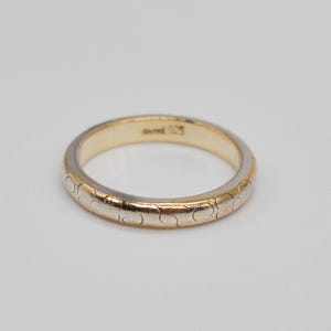 May include: A two-tone ring featuring a gold-coloured outer band with a repeating engraved swirl pattern and a smooth gold-coloured interior. The inner surface of the band is clearly stamped with the text 925, indicating its sterling silver composition.