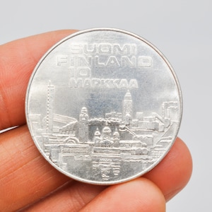 May include: A silver coin with the text "SUOMI FINLAND 10 MARKKAA" and a cityscape design.
