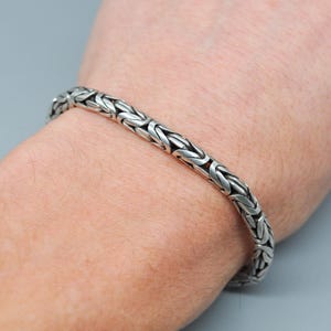Pode incluir: Um bracelete de corrente de prata com um design de corrente de caixa.