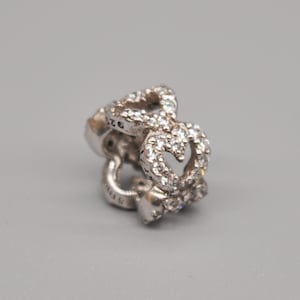 May include: Silver charm with a double heart design, featuring clear cubic zirconia stones. The charm is marked with "925" and "STERLING".