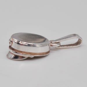 Puede incluir: Un colgante de plata pulida con forma de gorra clásica o sombrero de marinero. La pieza presenta una corona redondeada, una visera distintiva y una pequeña anilla en la parte posterior para colgarla de una cadena. La superficie es lisa y brillante.