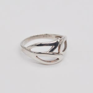 May include: A silver ring with an open, geometric design. The ring features a series of curved and angular shapes, creating an abstract pattern. The metal has a polished finish, reflecting light. This piece of jewelry is suitable for everyday wear.
