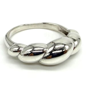 Puede incluir: Un anillo de plata pulida que presenta un diseño continuo, redondeado y trenzado similar a una cuerda que envuelve la banda. La superficie metálica es altamente reflectante, creando reflejos curvos y suaves en los segmentos abultados.
