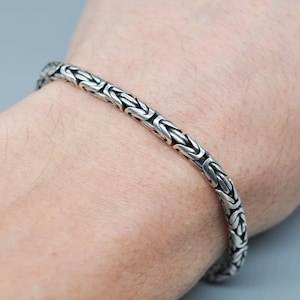 Pode incluir: Um bracelete de corrente de prata com um design de corrente de caixa.