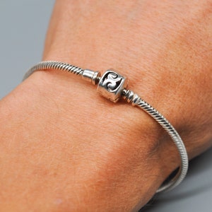 May include: A silver charm bracelet with a single charm featuring a stylised swirl design.