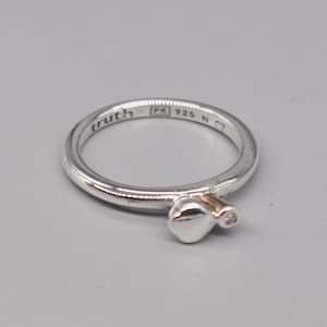 Könnte beinhalten: Ein silberner Ring mit einem herzförmigen Design und einem kleinen Diamanten. Der Ring ist mit "truth" und "PK 925 N" beschriftet.