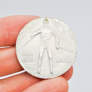 May include: Silver commemorative medal featuring a skier holding ski poles, with the text "MM 1978" and "LAHTI" on the medal.