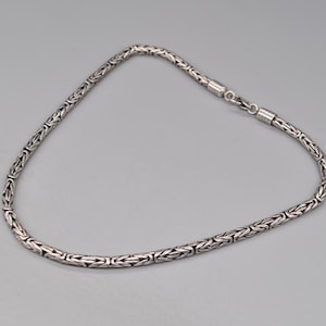 May include: A silver chain necklace with a box clasp. The chain is made of a woven pattern.