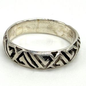 May include: A silver band ring featuring a continuous, repeating geometric pattern of recessed, dark-toned triangular and angular shapes carved into the outer surface, creating a textured contrast against the polished silver metal finish.