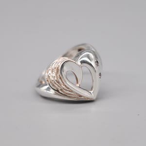 May include: A silver ring with a heart-shaped design. The heart is open in the center and has two small diamonds on the side.