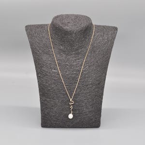 May include: A gold chain necklace with a pearl pendant and a gold swirl design.