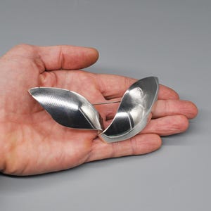 May include: A silver brooch with two curved, leaf-shaped pieces.