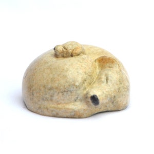 May include: A hand-carved stone sculpture of a dog curled up sleeping with a smaller dog on its back. The sculpture is made of a light beige stone with brown and black accents.