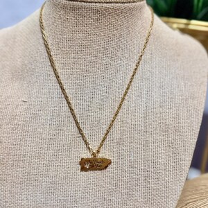 May include: Gold-toned necklace featuring a pendant shaped like the island of Puerto Rico. The pendant has the words "Puerto Rico" engraved on it. The necklace is displayed on a mannequin.