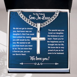 Könnte beinhalten: Halskette mit silbernem Kreuzanhänger in einer Geschenkbox. Die Halskette hat eine Panzerkette und einen polierten Kreuzanhänger. Die Box hat einen blauen Hintergrund mit Text, der lautet: "To Our Future Son-In-Law" und "We love you!"