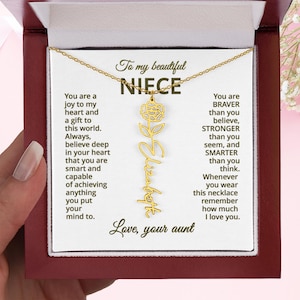 Può includere: Una collana color oro con il nome "Elizabeth" in corsivo e un ciondolo a forma di rosa. La collana è presentata in una confezione regalo rossa con un messaggio per una nipote.