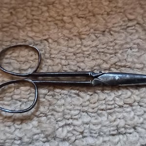 May include: A pair of antique silver-toned scissors with a long, pointed blade and two circular handles.