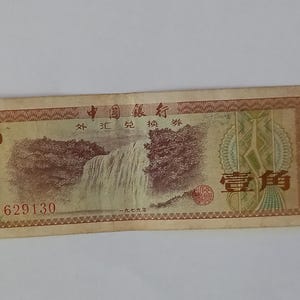 Könnte beinhalten: Ein chinesischer Banknote aus der Zeit mit einem braunen und grünen Design, das einen Wasserfall und Bäume zeigt. Die Banknote trägt den Text "中国银行" (China Bank) und "外汇兑换券" (Devisenwechselschein). Die Seriennummer "ZY 629130" ist in der linken unteren Ecke gedruckt. Die Banknote ist in gutem Zustand.