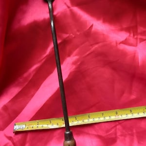 Puede incluir: Una herramienta larga y delgada de metal con un mango de madera. La herramienta tiene una hoja plana y rectangular en la parte superior y una punta puntiaguda en la parte inferior. La herramienta mide aproximadamente 23 cm de largo.