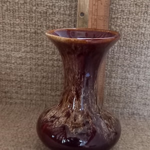 Könnte beinhalten: Eine kleine, braune und weiße, glasierte Keramikvase mit einer ausgestellten Öffnung und einem abgerundeten Boden.