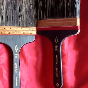 Puede incluir: Dos pinceles negros con detalles dorados y mangos de madera. Los mangos están etiquetados con "8oz. Acorn Black Knight" y "8oz. Acorn Black Knight".