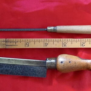 May include: Two vintage woodworking tools: a small hand saw with a wooden handle and a metal file with a wooden handle. Both tools have brass accents.