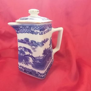 Könnte beinhalten: Eine blaue und weiße Porzellan-Teekanne mit quadratischem Korpus und Deckel. Die Teekanne zeigt ein traditionelles chinesisches Landschaftsdesign.