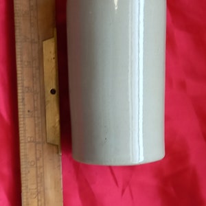Puede incluir: Una botella de cerámica con una tapa marrón y un cuerpo gris claro. La botella mide aproximadamente 25 cm de alto y tiene un diseño sencillo.
