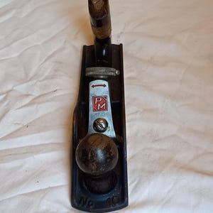 May include: A vintage wooden hand plane with a black metal body and a wooden handle. The plane is labeled "P.M. No. 10".
