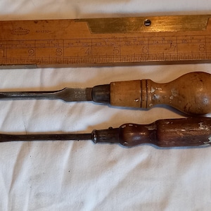 May include: Two vintage screwdrivers with wooden handles. The top screwdriver has a light brown handle and the bottom screwdriver has a dark brown handle.