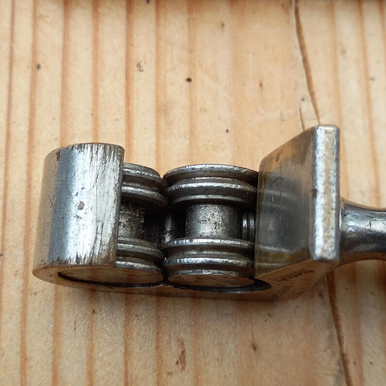 May include: Close-up of a silver metal chain breaker tool with a handle and a set of rollers. The tool is designed to break and connect bicycle chains.