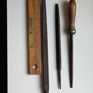 May include: Three metal files, two with pointed ends and one with a wooden handle. A wooden ruler with brass markings is also included.
