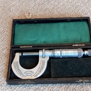 May include: A silver micrometer with a black leather case. The micrometer has a scale marked in inches and a dial marked in thousandths of an inch. The case has a green felt lining.