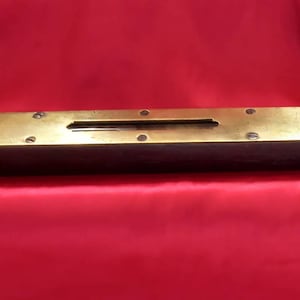 Puede incluir: Un nivel de burbuja de latón con una base de madera. El nivel tiene una ampolla de nivel de latón y está asegurado con tornillos.