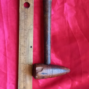 May include: A wooden mallet with a rounded head and a long handle. The mallet is approximately 15 cm long and is made of dark brown wood. The mallet is next to a brass ruler with markings in inches.
