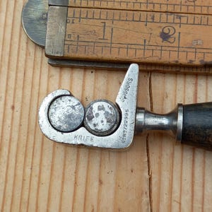 May include: A silver metal tool with a black handle for sharpening scissors and knives. The tool has the words "KNIFE" and "SCISSORS" engraved on it, along with the number "RBN 9722996".