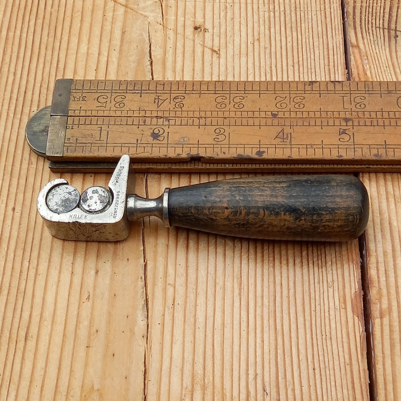 May include: A vintage metal and wood tool with a wooden handle. The tool has two metal rollers and the text "SELF CENTERING" and "KNIFE" is visible on the metal part.