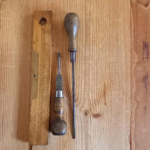 Könnte beinhalten: Zwei vintage Schraubendreher mit Holzgriffen und Metallklingen sowie ein Holzlinienschieber mit Messingmarkierungen.