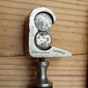 May include: A silver-toned metal tool with a handle and two circular cutting blades. The tool is labeled "KNIFE" and "SCISSORS" and has the number "722996" printed on it.