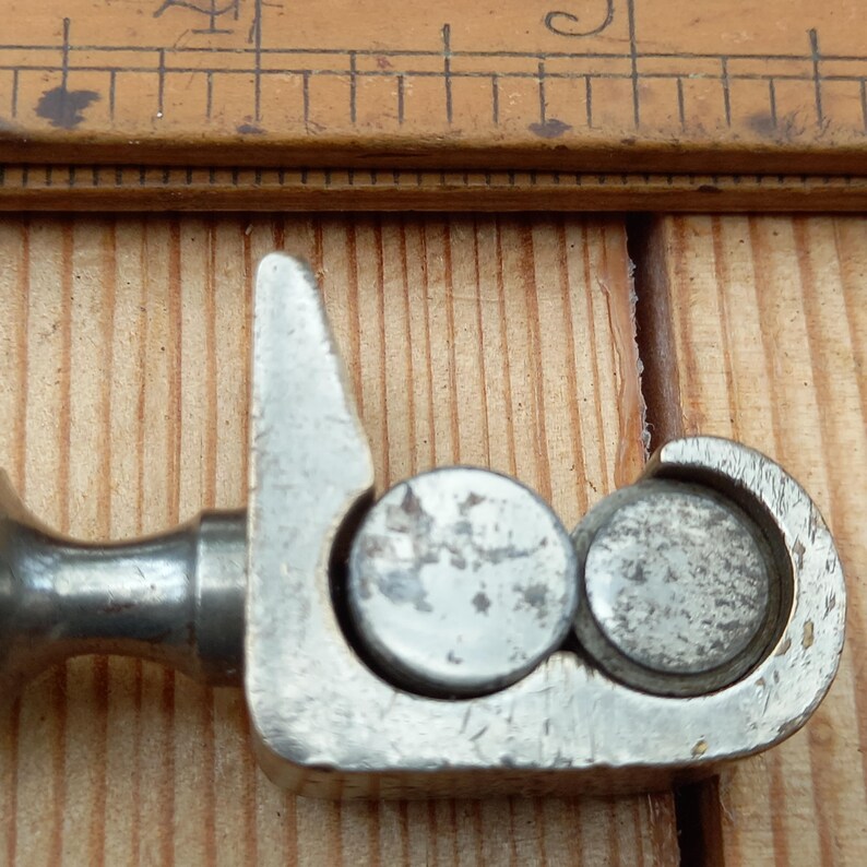 May include: Close-up of a silver metal tool with two round knobs. The tool has a curved handle and a pointed end.