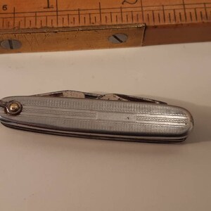 May include: A silver pocket knife with a gold accent on the handle. The knife has multiple blades and is closed.