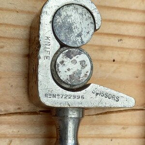 May include: A silver metal tool with two circular blades and a handle. The tool is labeled "KNIFE" and "SCISSORS" and has the number "RD.NO.722996" engraved on it.