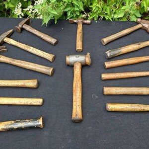 May include: A collection of 13 vintage hammers with wooden handles. The hammers are arranged in a semi-circle on a black surface. The hammers are all different sizes and shapes, and some have different head designs.