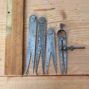 May include: Set of five antique metal calipers, including a pair of adjustable calipers. The calipers are made of silver-toned metal and have a worn, aged appearance.
